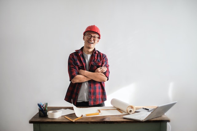 person in a hardhat and flannel smiling in front of their work bench